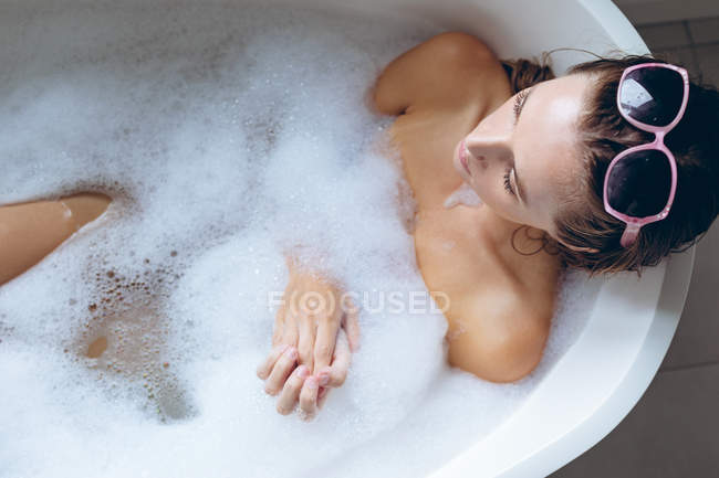 Gros plan sur une jeune femme portant des lunettes de soleil se relaxant dans la baignoire — Photo de stock