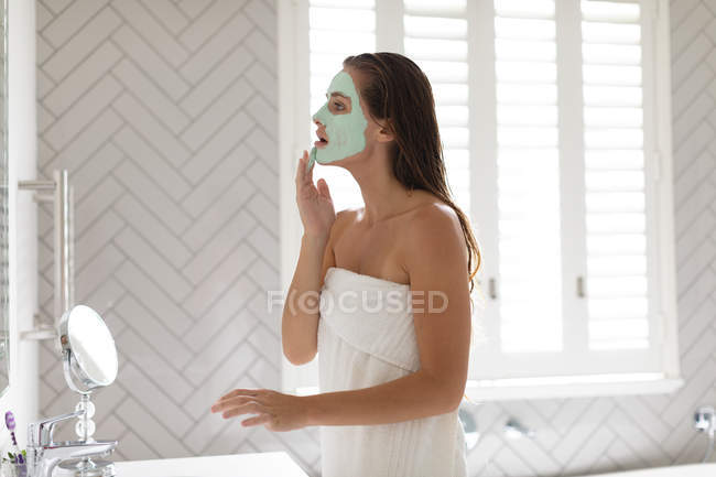 Vue latérale de la femme appliquant un masque facial dans la salle de bain après le bain — Photo de stock