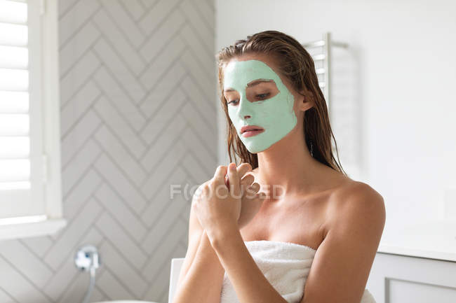 Gros plan de femme réfléchie avec masque facial assis dans la salle de bain — Photo de stock