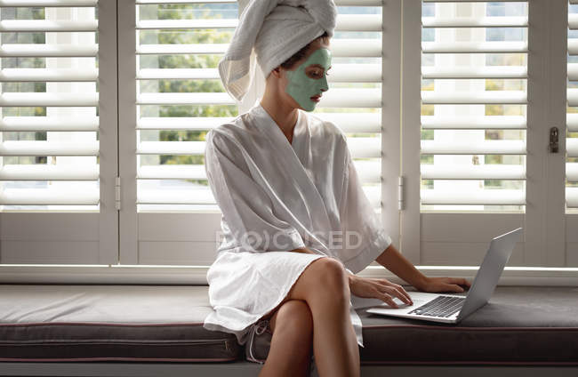 Mulher de roupão de banho usando um laptop perto da janela em casa — Fotografia de Stock