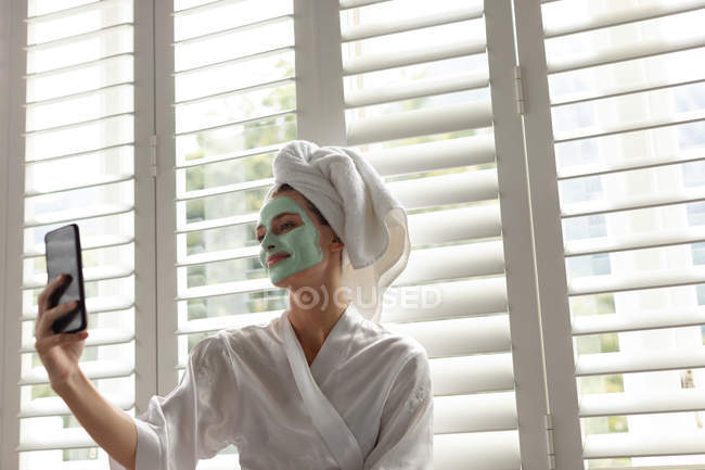 Mulher sorridente em roupão de banho tirando uma selfie em casa — Fotografia de Stock