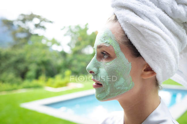 Vue latérale de la femme dans le masque facial regardant loin près de la piscine — Photo de stock