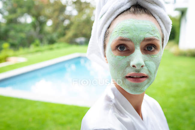 Портрет женщины в маске для лица, смотрящей в камеру возле бассейна — стоковое фото