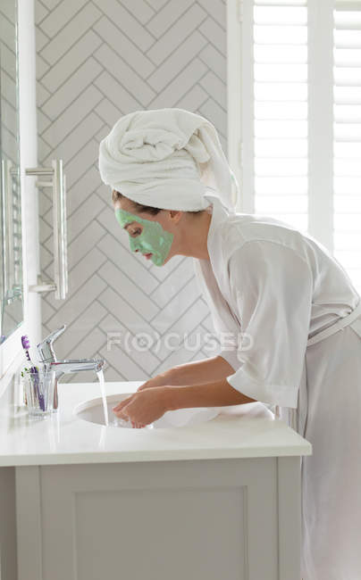 Vista lateral mulher lavando sua máscara facial na pia do banheiro em casa — Fotografia de Stock