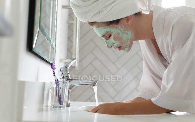Vista laterale donna che lava la maschera nel lavandino del bagno a casa — Foto stock