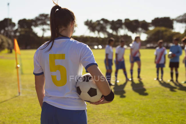 Vista trasera de la jugadora asiática con pelota de pie en el campo de deportes en un día soleado - foto de stock