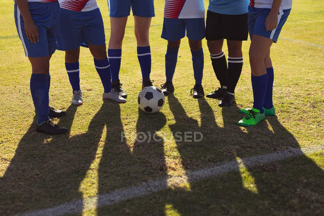 Seção média de jogadoras de futebol se preparando para jogar futebol no campo de esportes em um dia ensolarado — Fotografia de Stock