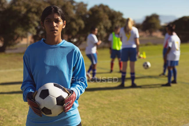 Портрет індійського жіночого футболіста з м'ячем стоячи на спортивному полі в сонячний день — стокове фото