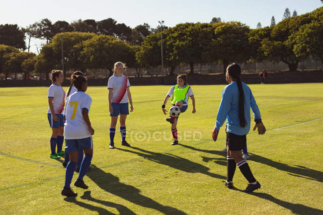 Вид сзади на разнообразную женщину-футболистку, играющую в футбол на спортивной площадке в солнечный день — стоковое фото
