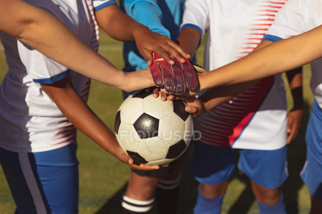 Средняя секция женщин-футболистов формирует стопку рук на спортивной площадке в солнечный день — стоковое фото