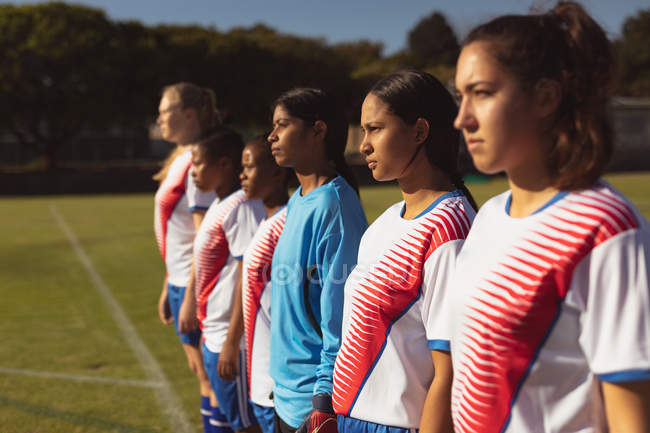 Vista lateral de diversas jogadoras de futebol que estão em fila no campo de esportes no dia ensolarado — Fotografia de Stock