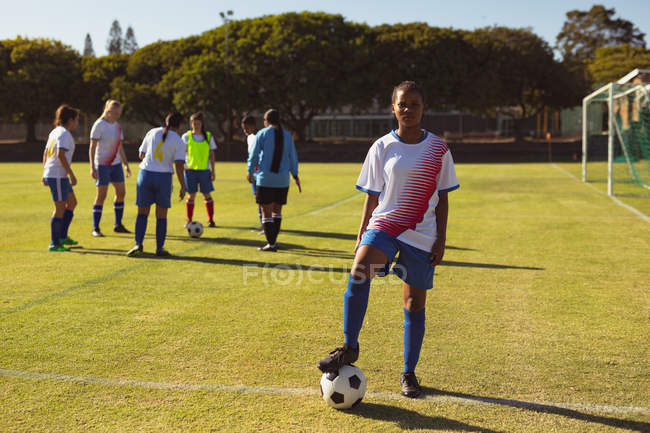 Retrato de una futbolista diversa con pelota en el campo de deportes en un día soleado - foto de stock