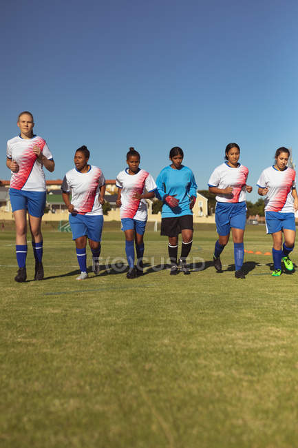 Вид спереди на разнообразных женщин-футболистов, бегающих на спортивной площадке в солнечный день — стоковое фото