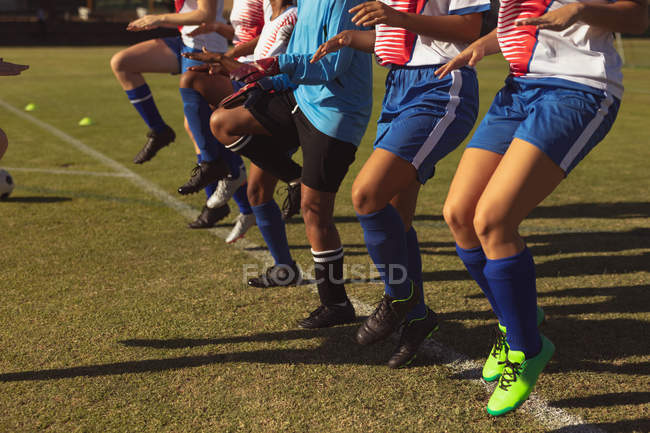 Seção média de jogadores de futebol do sexo feminino aquecendo no campo de esportes em um dia ensolarado — Fotografia de Stock