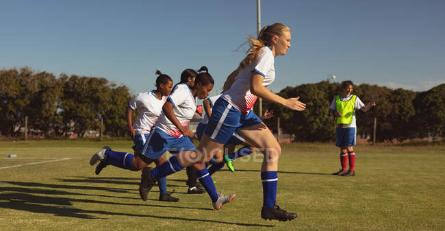 Side view of diverse women soccer players running at sports field on a sunny day — стоковое фото