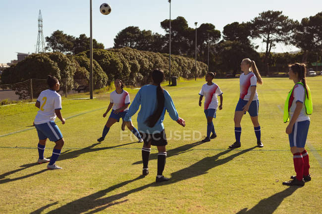 Rear view of diverse female soccer players practicing soccer at sports field on a sunny day — Stock Photo