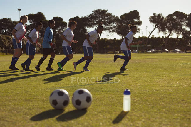 Вид збоку на різноманітних футболісток, що працюють у лінії на спортивному полі в сонячний день . — стокове фото