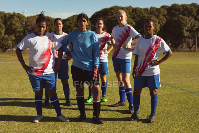 Vista frontal de diversas jogadoras de futebol olhando para a câmera no campo de esportes em um dia ensolarado — Fotografia de Stock