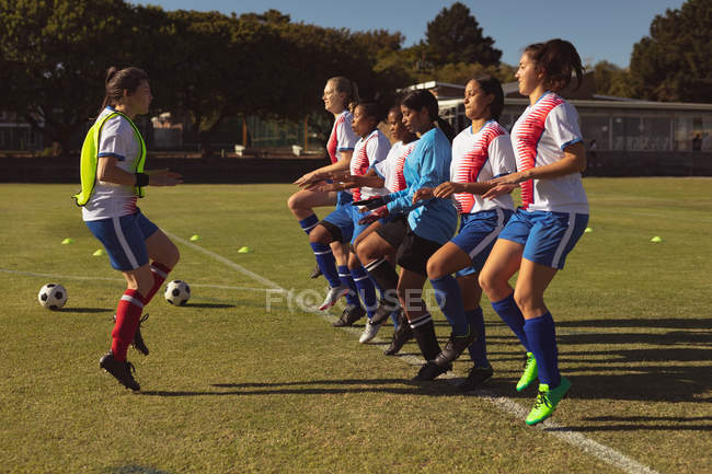 Side view of diverse female soccer players warming up at sports field on a sunny day — Stock Photo