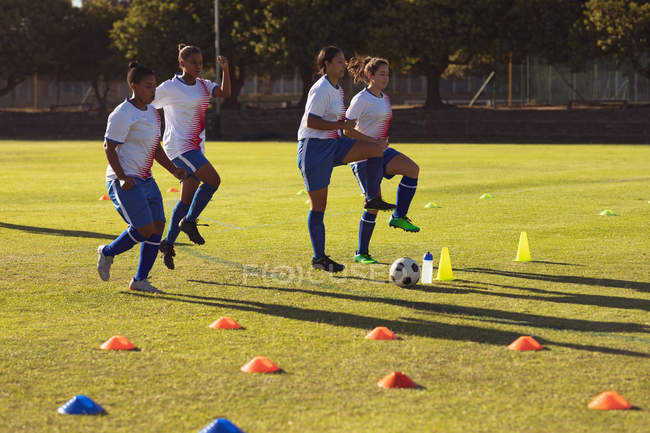Vue latérale de diverses joueuses de soccer faisant de l'exercice d'échauffement sur le terrain par une journée ensoleillée — Photo de stock