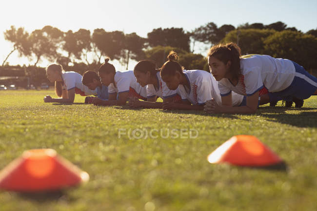 Вид сбоку на команду разноплановых футболистов, работающих на спортивной площадке в солнечный день — стоковое фото