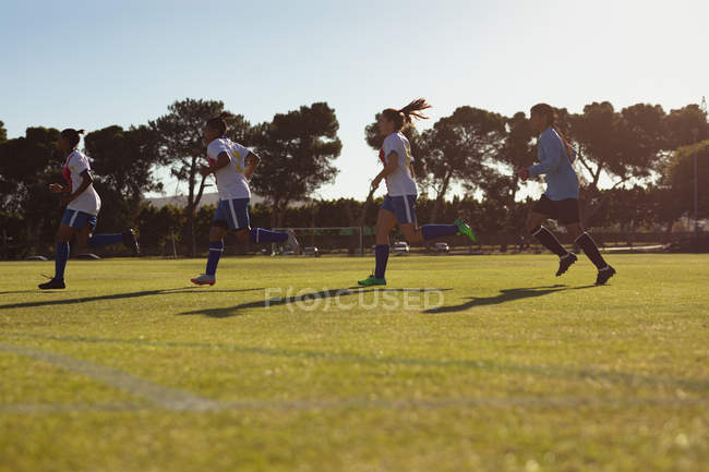 Visão de baixo ângulo de diversas jogadoras de futebol que correm no campo de esportes em um dia ensolarado — Fotografia de Stock