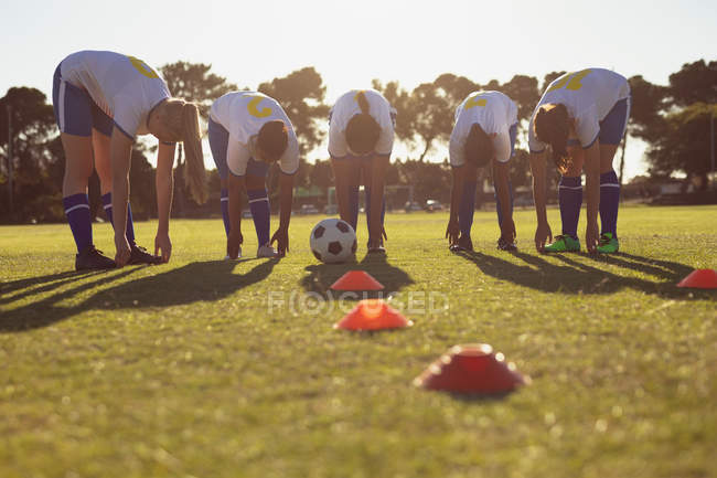 Front view of diverse women soccer players doing warm-up exercise on the field on a sunny day — стоковое фото
