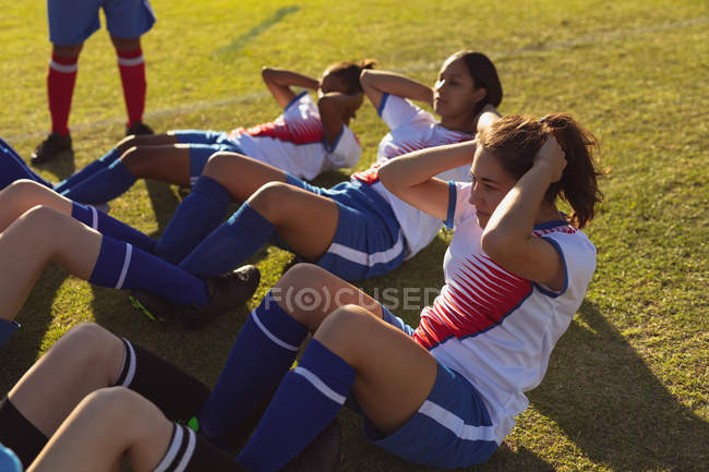 Vista de ángulo alto de determinadas jugadoras de fútbol diversas haciendo abdominales en el campo en un día soleado - foto de stock