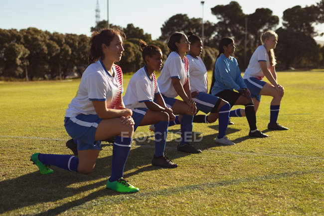 Side view of diverse female soccer players doing warm-up exercise on the field on a sunny day — Stock Photo