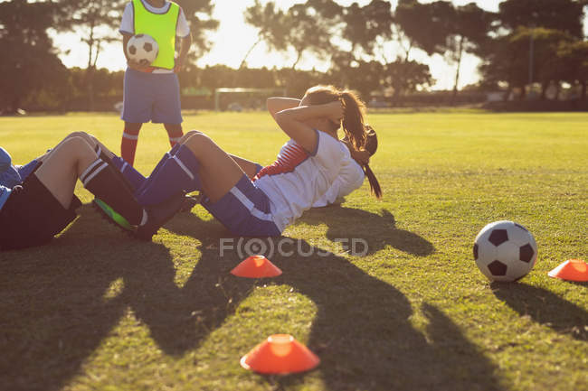 Side view of determined diverse female soccer players doing crunches on the field on a sunny day — Stock Photo