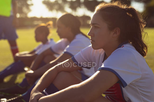 Vista lateral de determinadas diversas jogadoras de futebol sentadas no campo de esportes em um dia ensolarado — Fotografia de Stock