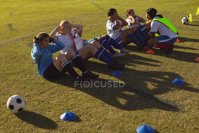 Высокий угол обзора различных женщин-футболистов, делающих хрусты на спортивной площадке в солнечный день — стоковое фото