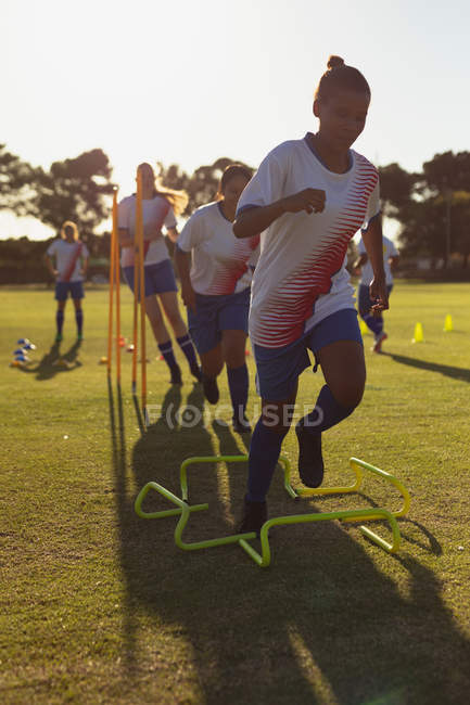 Front view of diverse female soccer players jumping over the hurdle during the training on field — Stock Photo