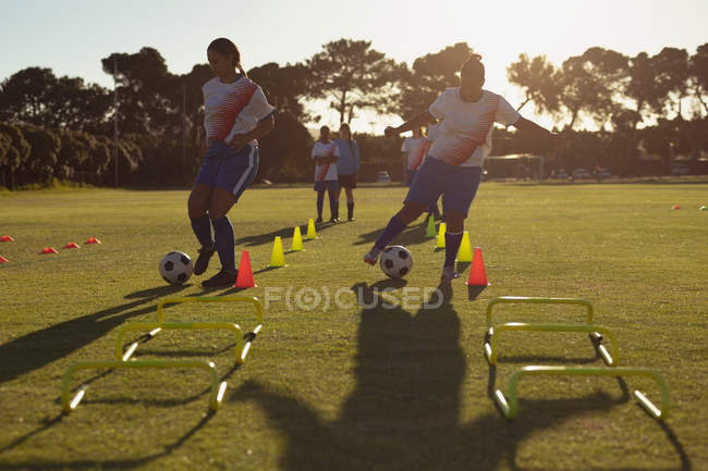 Vista frontal de diversas jogadoras de futebol passando a bola entre os cones durante o treinamento em campo — Fotografia de Stock