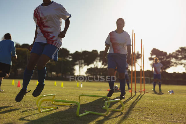 Low angle view of diverse female soccer players jumping over hurdle during the training at sports field on a sunny day — Stock Photo