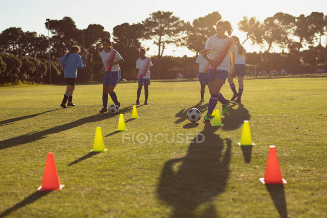 Передній план різноманітних футболісток, які проходять м'яч між конусами під час тренування на полі — стокове фото