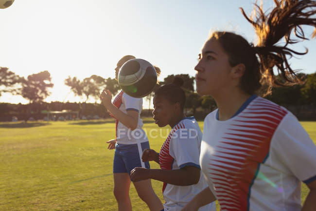 Vista lateral de diversas jugadoras de fútbol que golpean la pelota con la cabeza mientras practican en el campo - foto de stock
