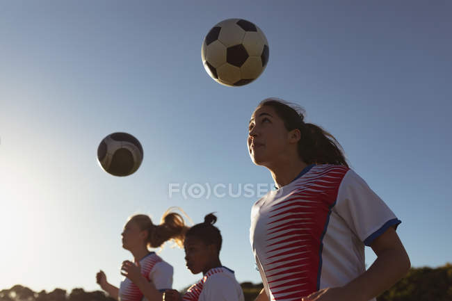 Low angle view of diverse female soccer players hitting the ball with head while practicing on the field — Stock Photo