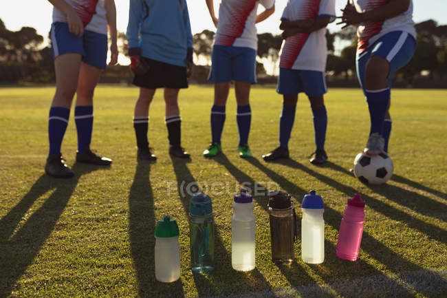 Вид спереди на бутылки с водой, стоящие в ряд перед футболистками на поле — стоковое фото