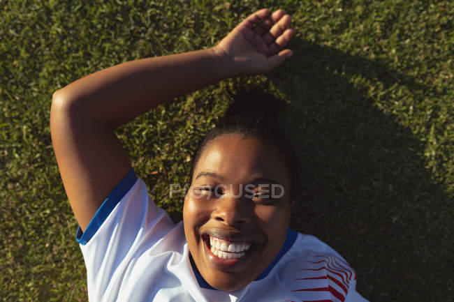 Portrait of happy African-american female soccer player relaxing on the field on a sunny day — Stock Photo