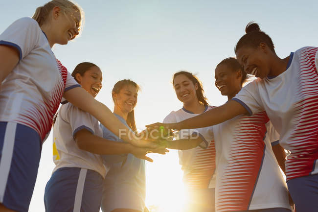 Низкий угол обзора счастливых разнообразных женщин-футболистов, формирующих стопку рук на поле в солнечный день — стоковое фото