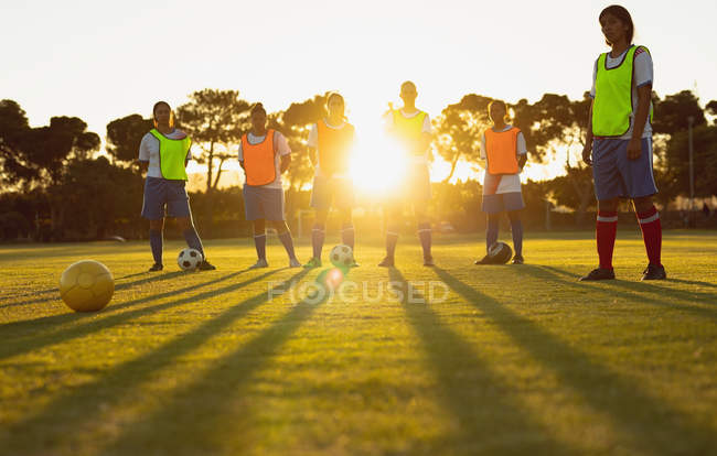 Низкий угол обзора различных женщин-футболистов, стоящих вместе на спортивной площадке в сумерках — стоковое фото