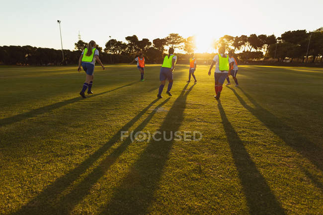 Rear view of diverse female soccer players playing at sports field at dusk — Stock Photo