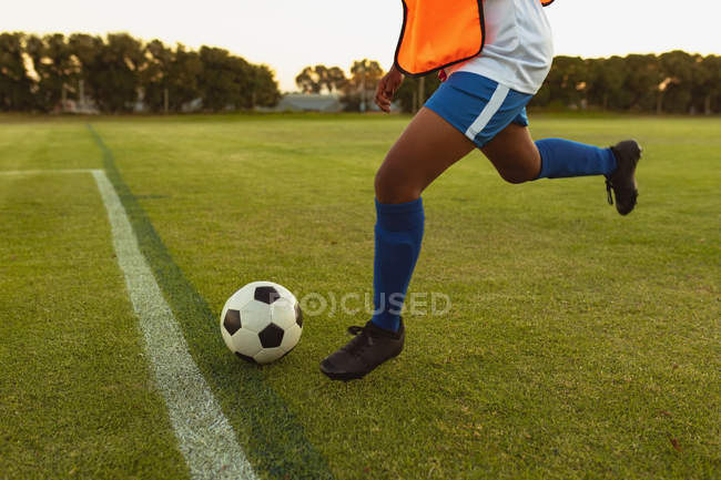 Baixa seção do jogador de futebol feminino chutando bola da linha de marcação no campo de esportes — Fotografia de Stock
