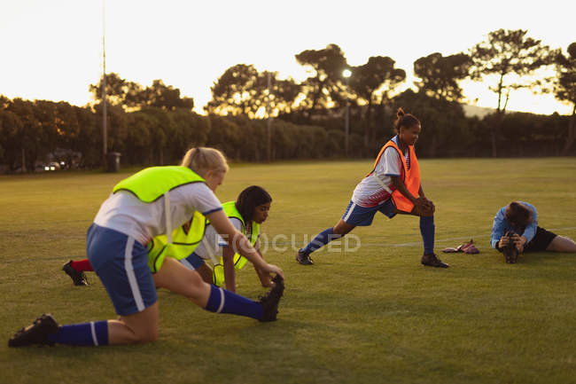Vista frontal de diversas jogadoras de futebol fazendo exercício de aquecimento no campo esportivo durante o torneio — Fotografia de Stock