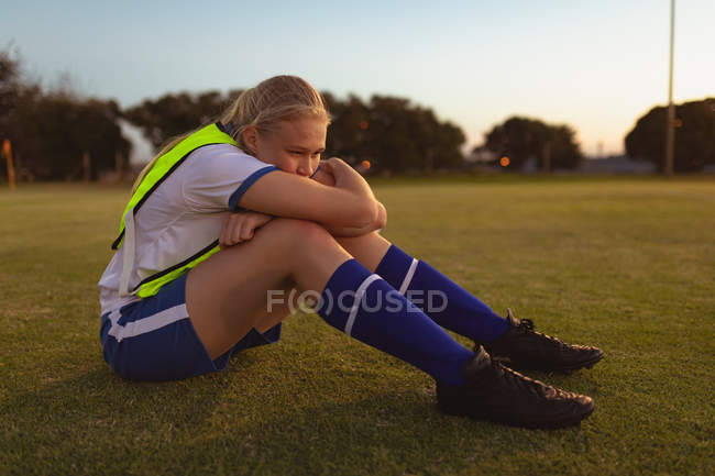 Vista lateral do jogador de futebol feminino caucasiano relaxando na grama no campo de esportes — Fotografia de Stock