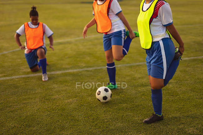 Side view of diverse female soccer players doing warm-up exercises at sports field during tournament. — Stock Photo