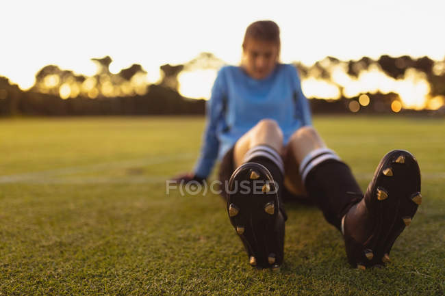 Vista frontal del cansado jugador de fútbol femenino caucásico relajándose en la hierba en el campo de deportes - foto de stock