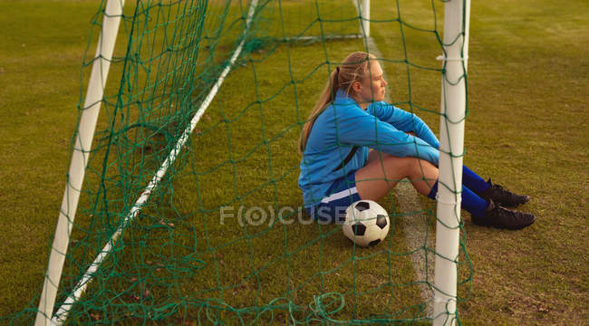 Задумчивая кавказская футболистка отдыхает на спортивной площадке — стоковое фото