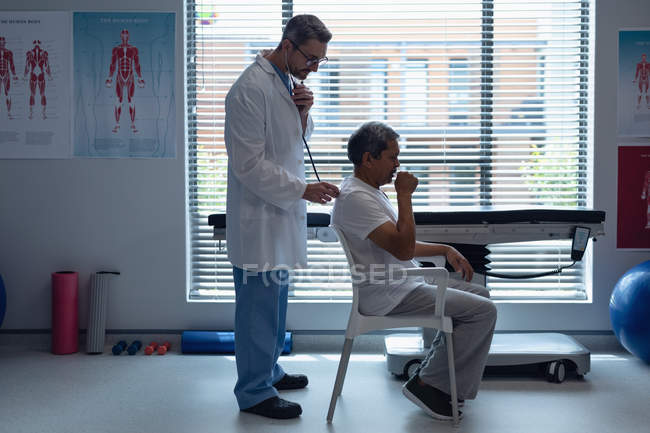Side view of Caucasian male doctor examining senior mixed race male patient with stethoscope in hospital — Stock Photo